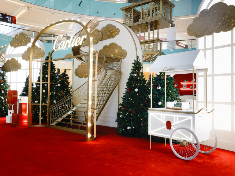 Cartier festive installation with a gold arch, red carpet, decorated trees and a white cart